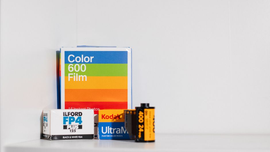 A collection of photographic and film materials arranged on a white surface against a plain white background. Included are a box of Ilford FP4 Plus black and white film, a Kodak Ultra Max 400 24 expos